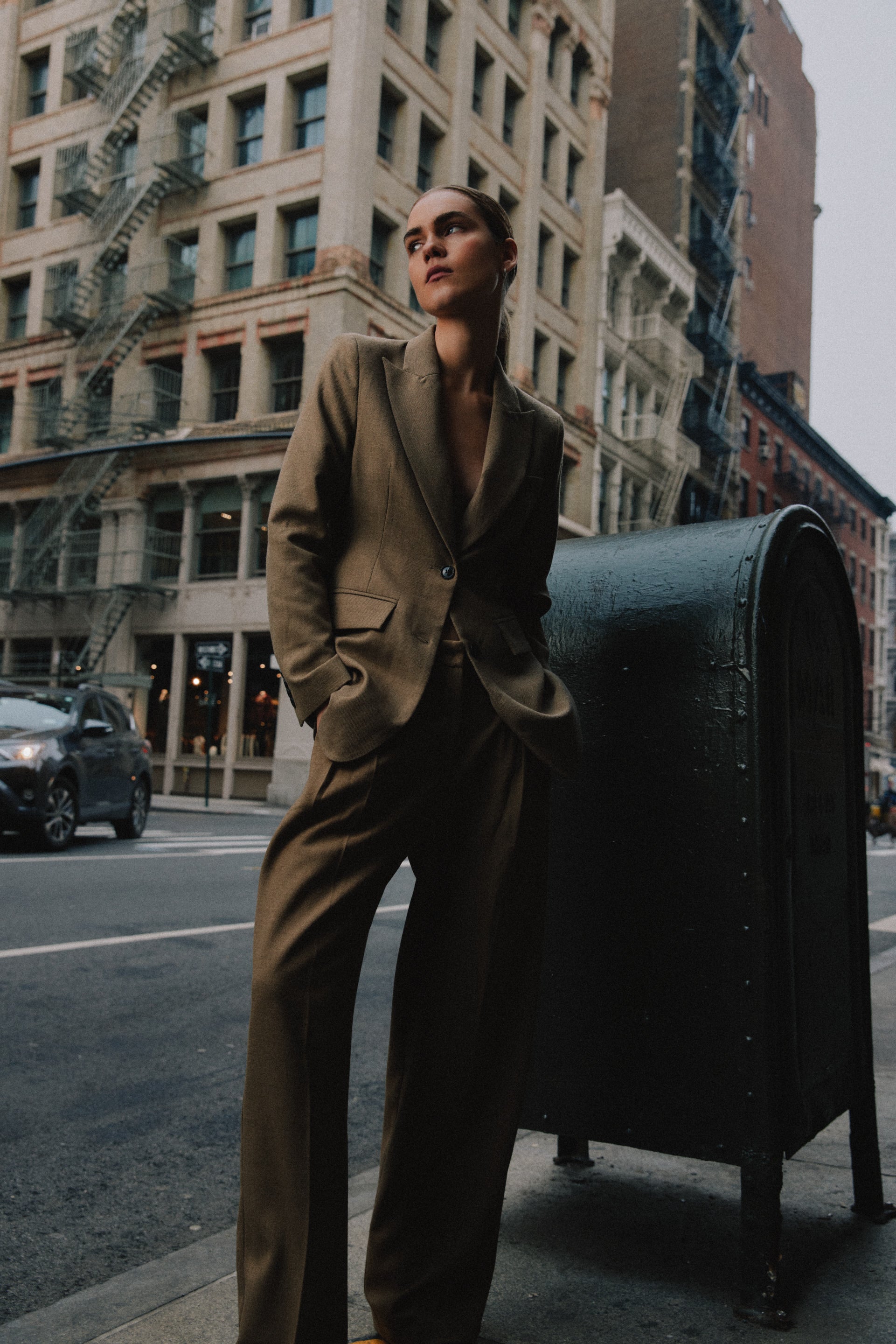 Femme en blazer beige appuyée contre une boîte aux lettres dans les rues de New York.