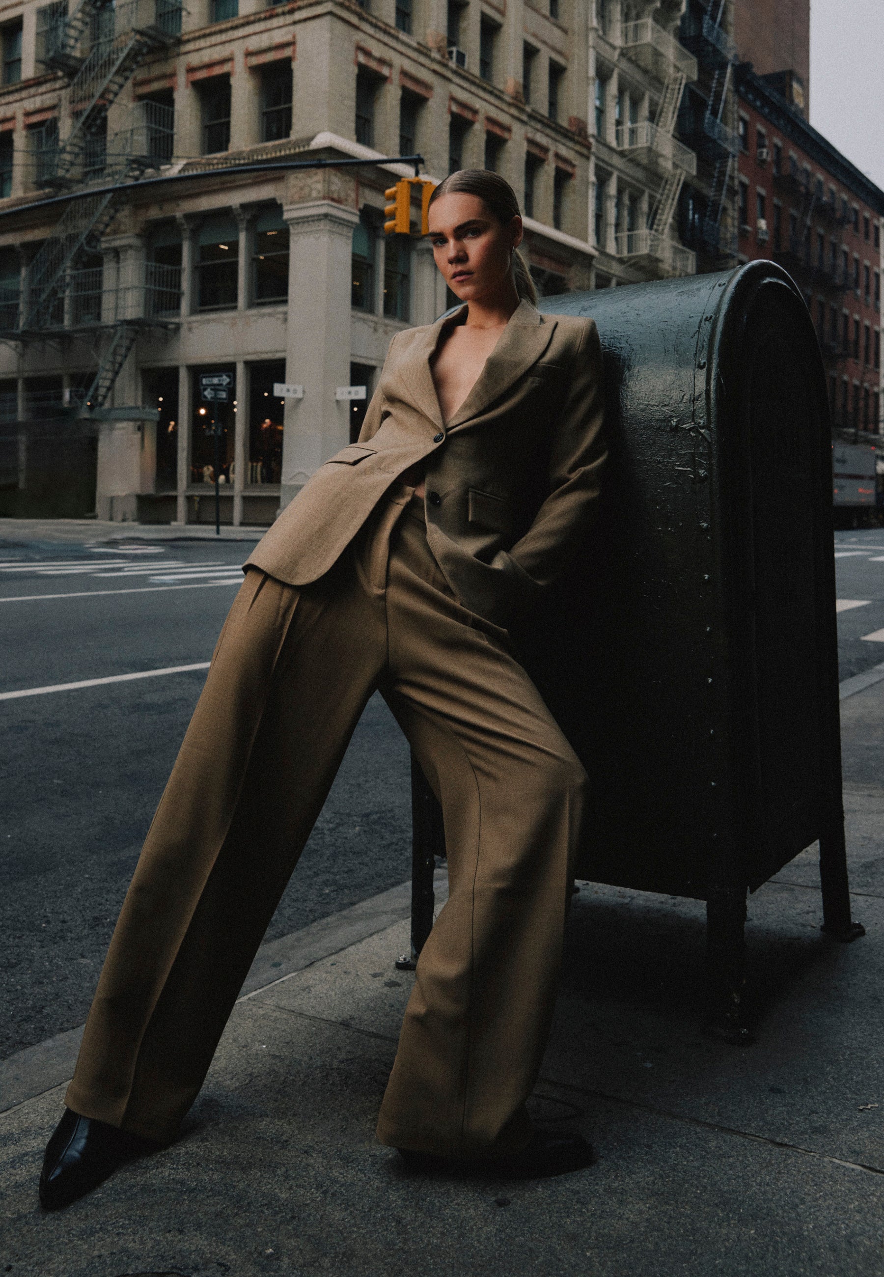 Femme en blazer beige appuyée contre une boîte aux lettres dans les rues de New York.